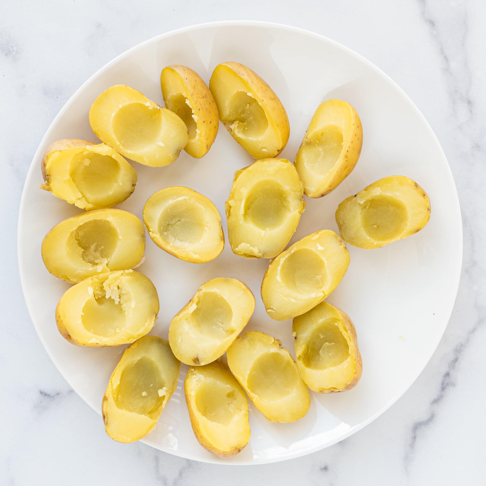 A plate of baby potatoes cut in half with the center scooped out.