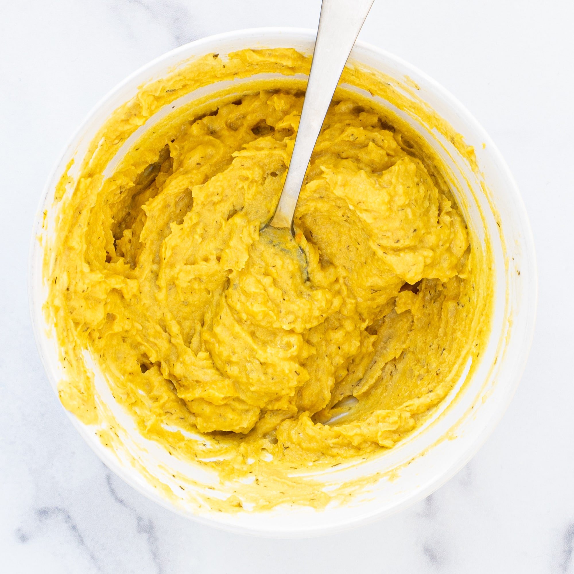 A bowl of a yellow mashed potato filling with a spoon sticking out.