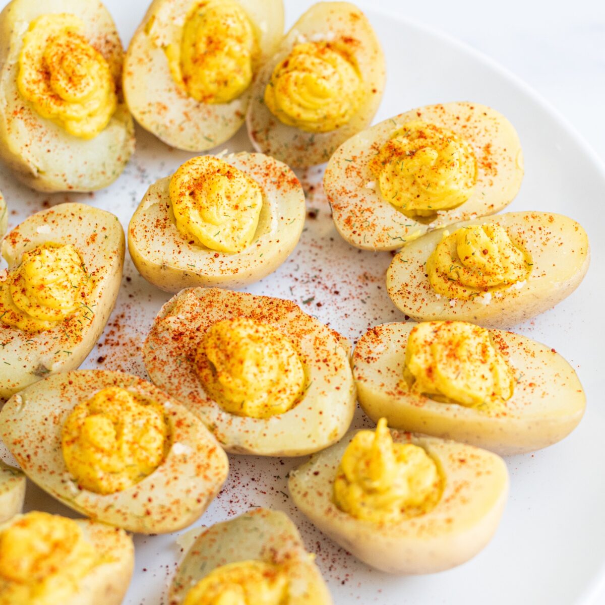 A plate of vegan deviled eggs made from potatoes sprinkled with paprika.