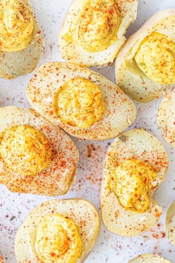 A plate of vegan deviled eggs made from potatoes sprinkled with paprika.