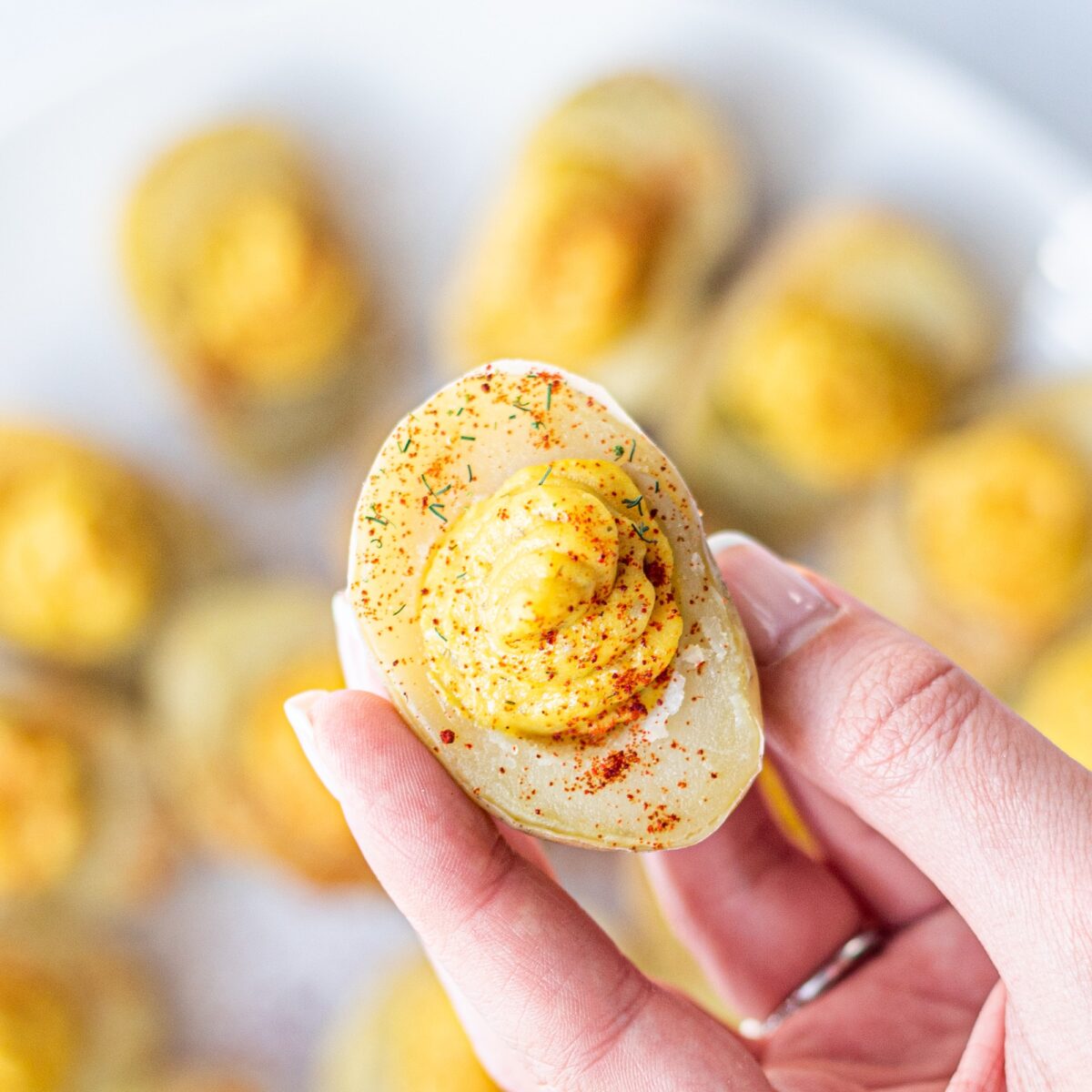 A hand holding a vegan deviled egg (made from potato) sprinkled with paprika.