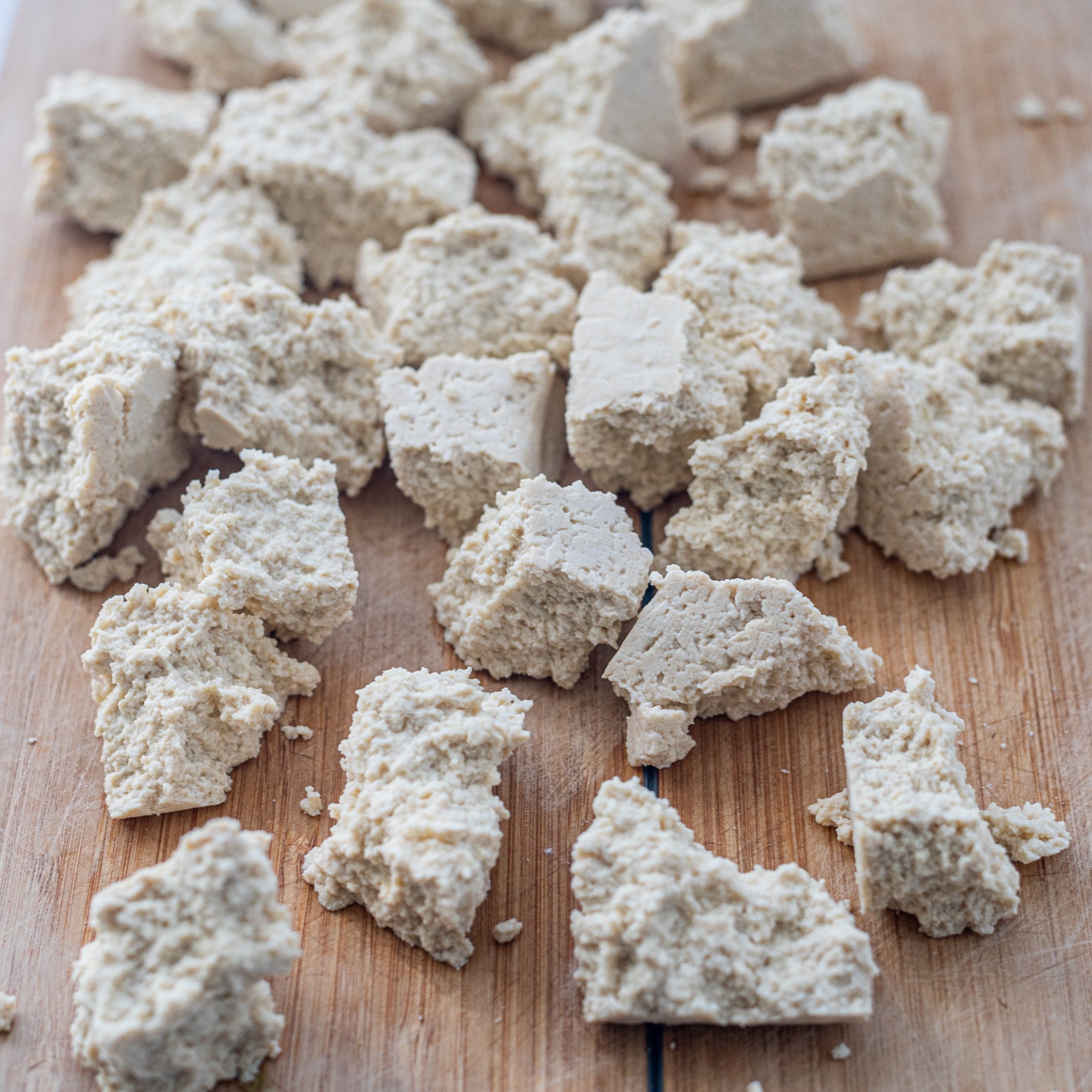 Wooden cutting board with tofu pieces on it.