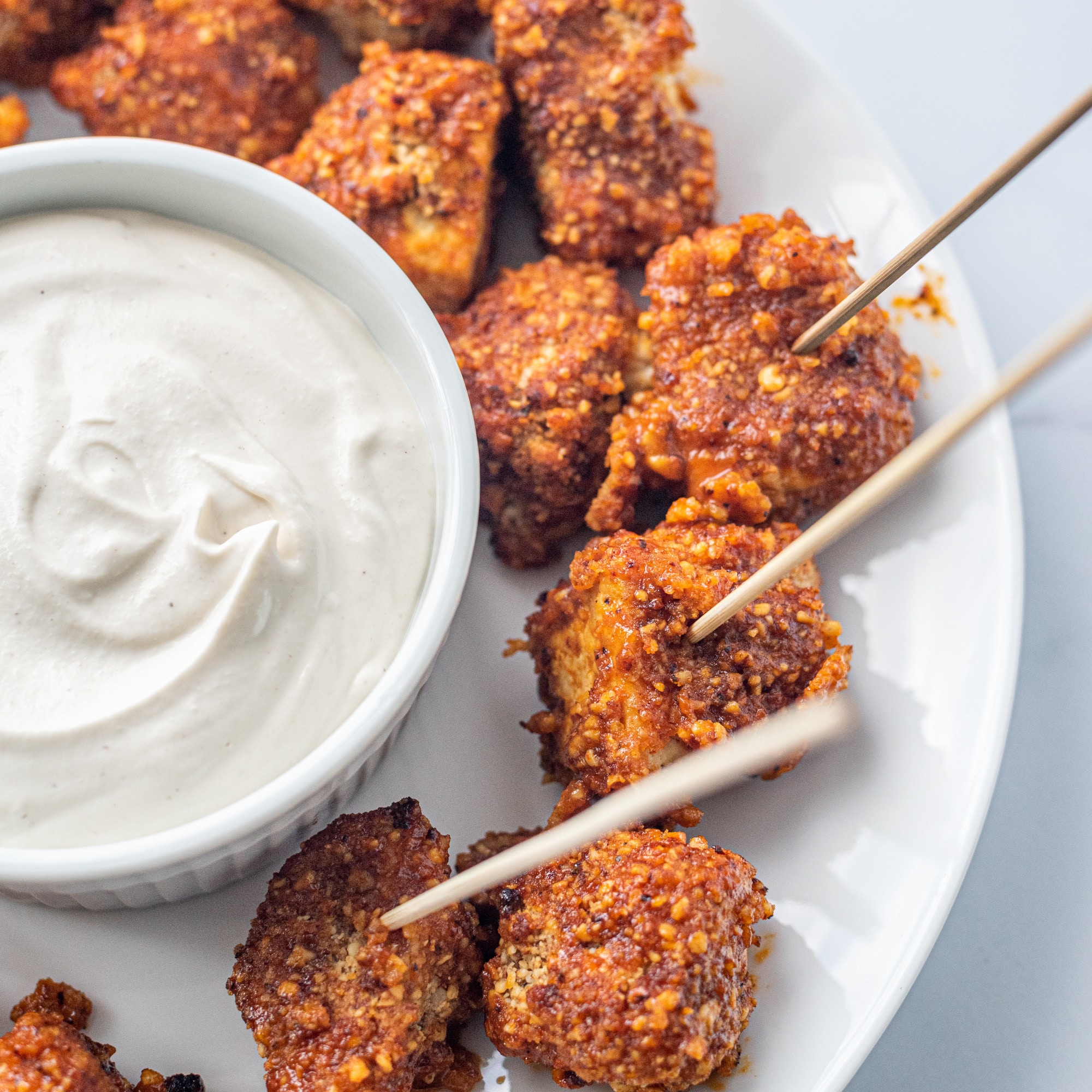 A white plate with buffalo tofu poppers and a bowl of sour cream on it.
