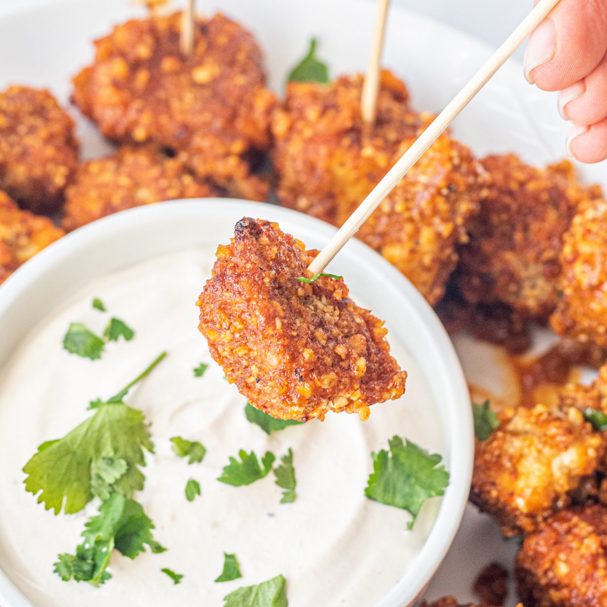 A white plate with buffalo tofu poppers and a bowl of sour cream all garnished with fresh cilantro.