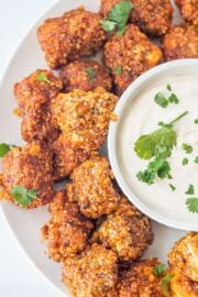 A plate of buffalo tofu poppers with a dip in the center with cilantro.