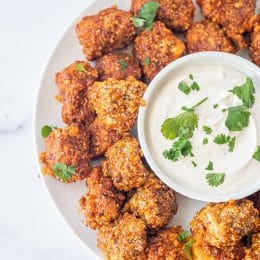 A plate of buffalo tofu poppers with a dip in the center with cilantro.