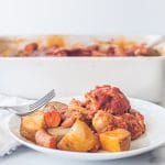 A plate with carrots, potatoes, and jackfruit brisket on in covered in a tomato sauce with a fork.