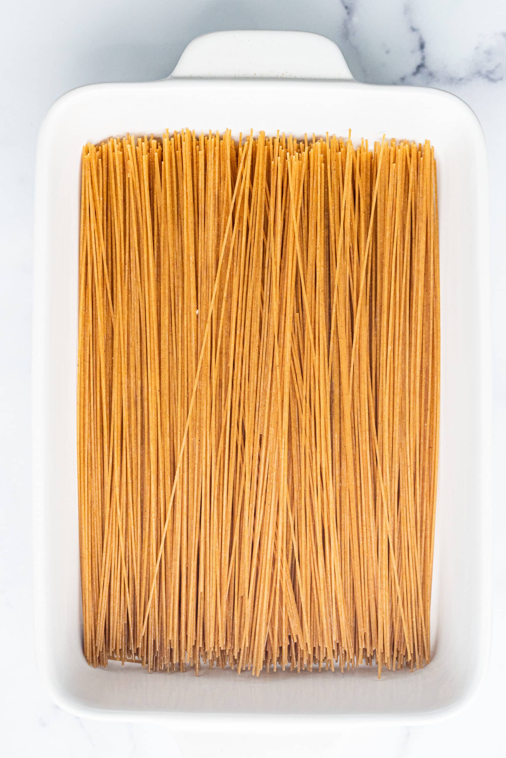 A white glass 9x13 casserole dish filled with dry spaghetti noodles.