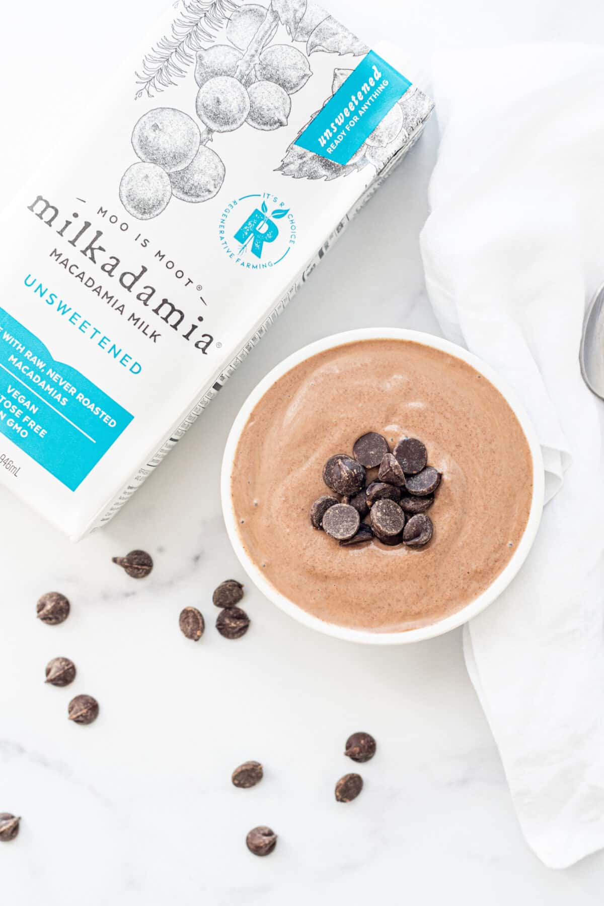 A bowl of chocolate mousse topped with chocolate chips and a carton of macadamia milk.