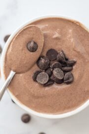 A bowl of Vegan Tofu Chocolate Mousse topped with chocolate chips and a spoon sticking out of the bowl.