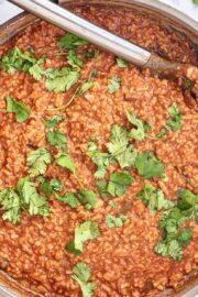 One Pan Creamy Mexican Cauliflower Rice garnished with fresh cilantro in a large pot with a silver spoon in it. Around the pot is cilantro leaves laying on the counter.