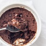 A white bowl of chocolate mug cake with a spoon in the center and a bite scooped out on the spoon.