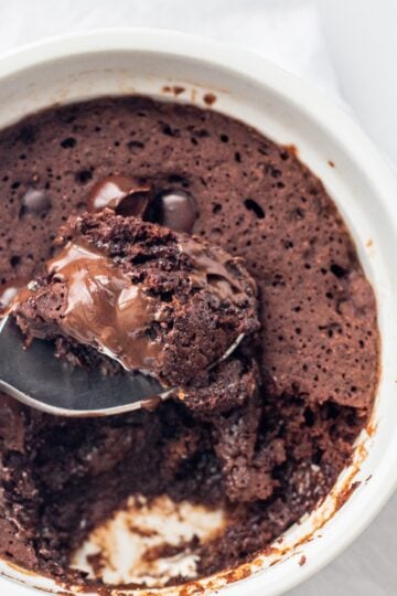 A white bowl of chocolate mug cake with a spoon in the center and a bite scooped out on the spoon.