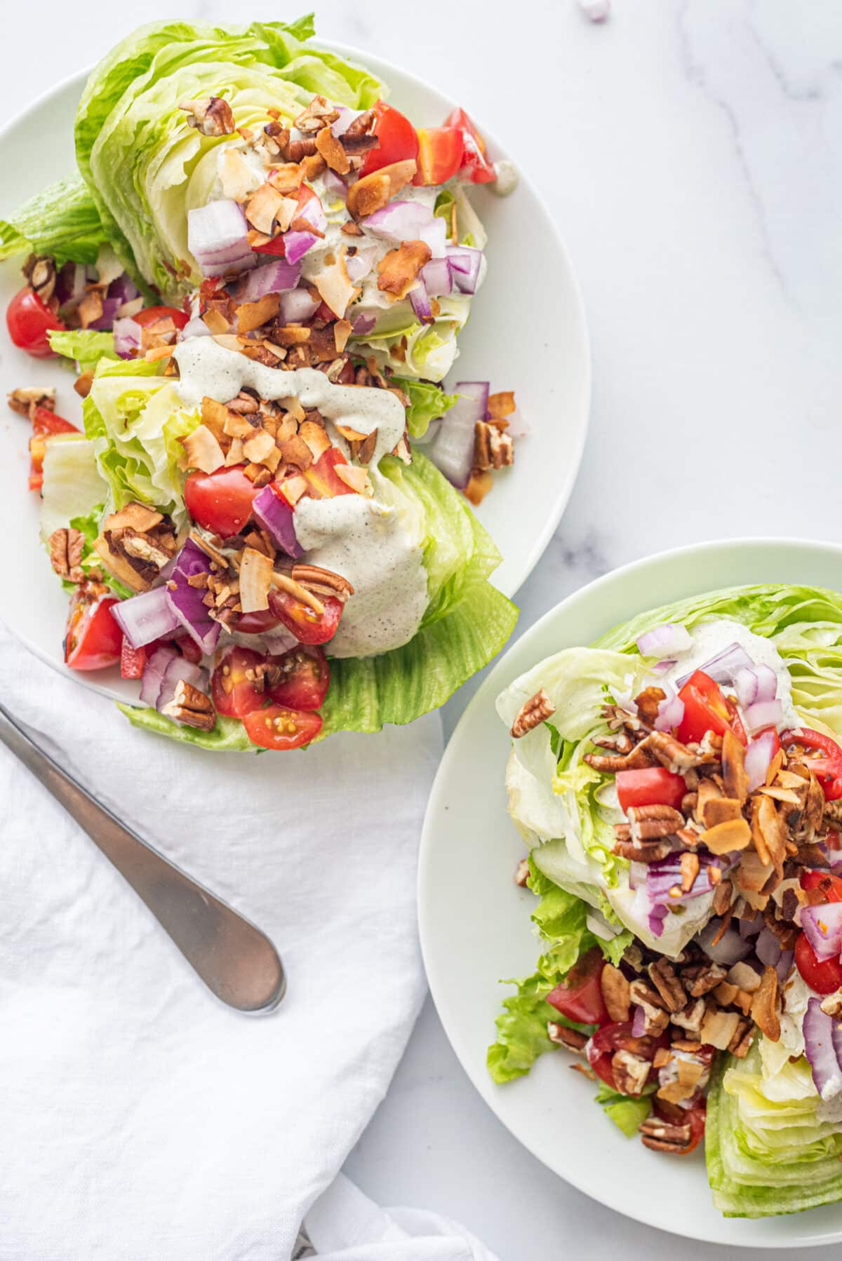 Two plates of wedge salad and a silver fork on a white napkin.