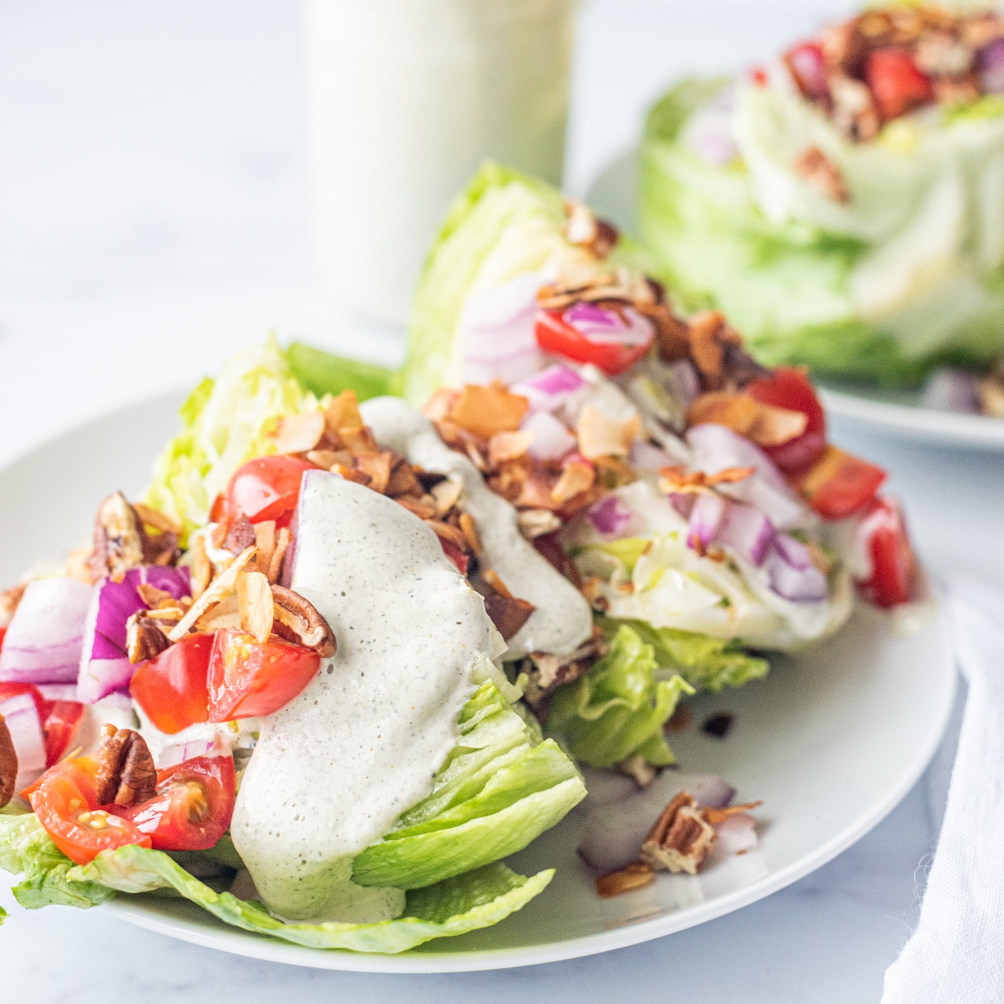 A plate of a wedge salad and in the background is another plate with salad and a glass jar of hemp ranch.