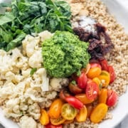 A white bowl filled with vegan mediterranean couscous salad and a wood tong.