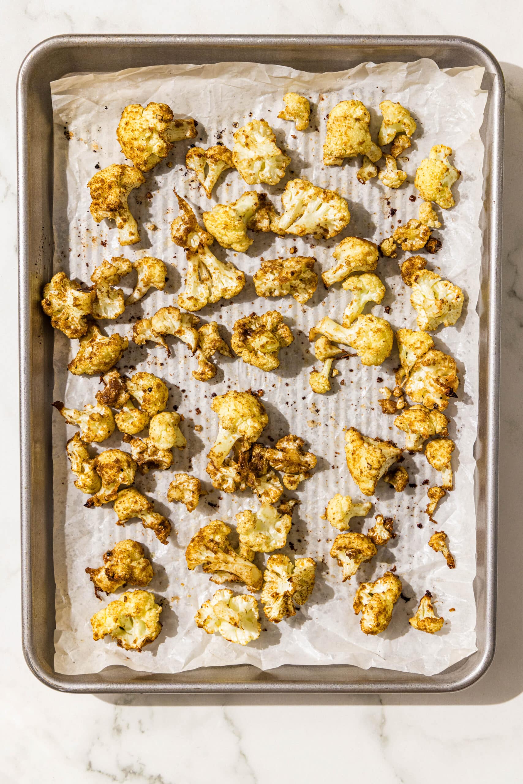 A silver baking sheet lined with parchment paper with roasted cauliflower on it.