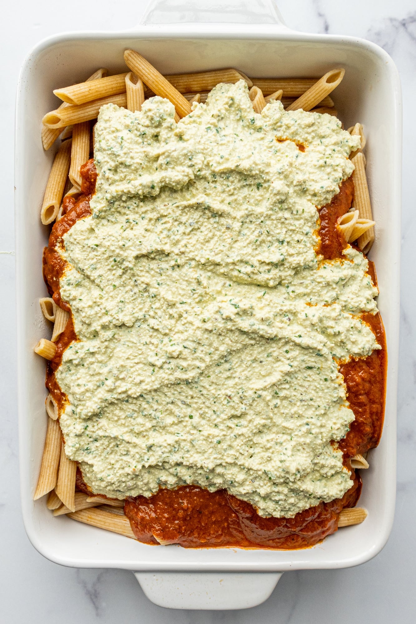 A 9x13 casserole dish filled with pasta noodles, marinara, and tofu ricotta on top.