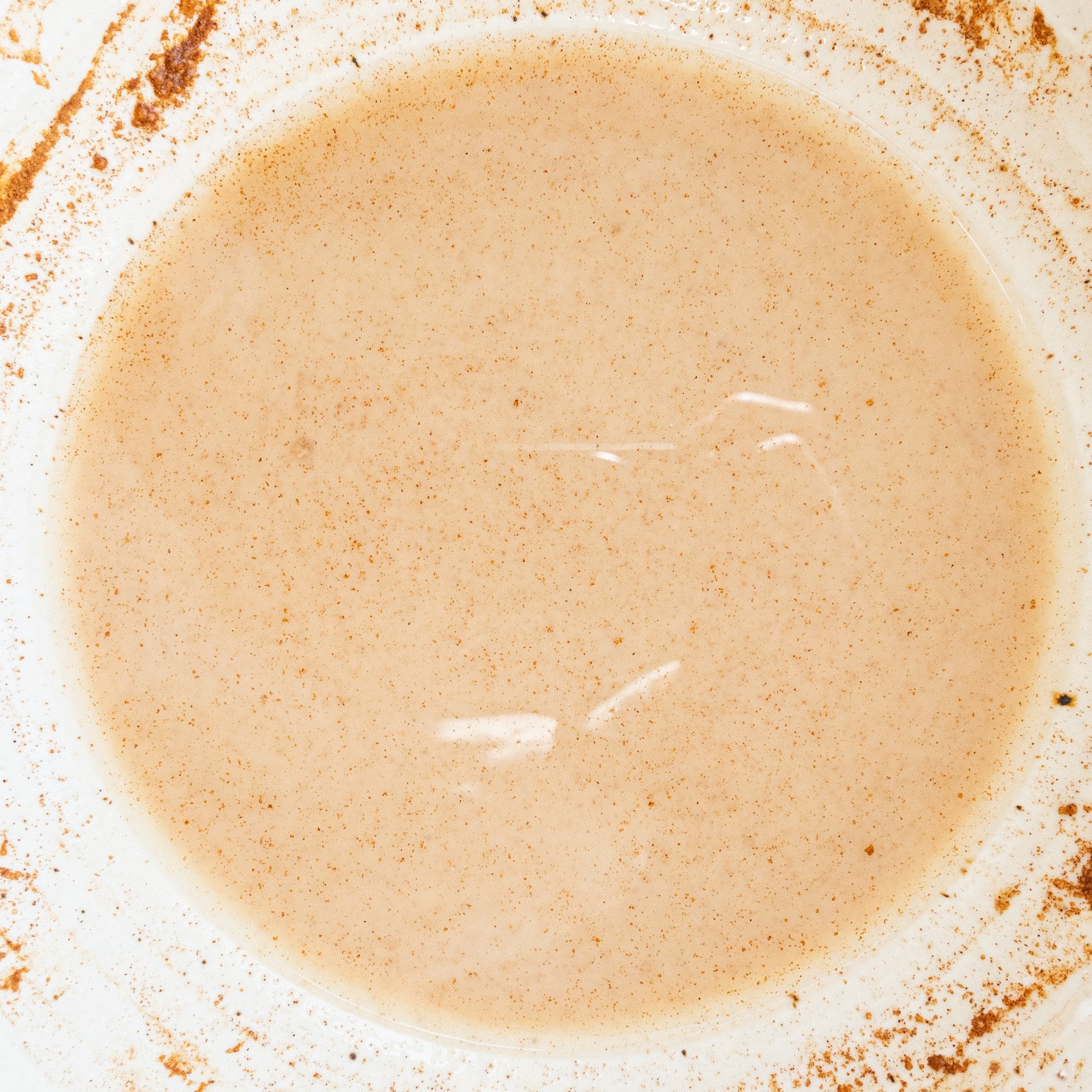 A white bowl with almond milk, maple syrup, corn starch, cinnamon, and vanilla in it mixed together.