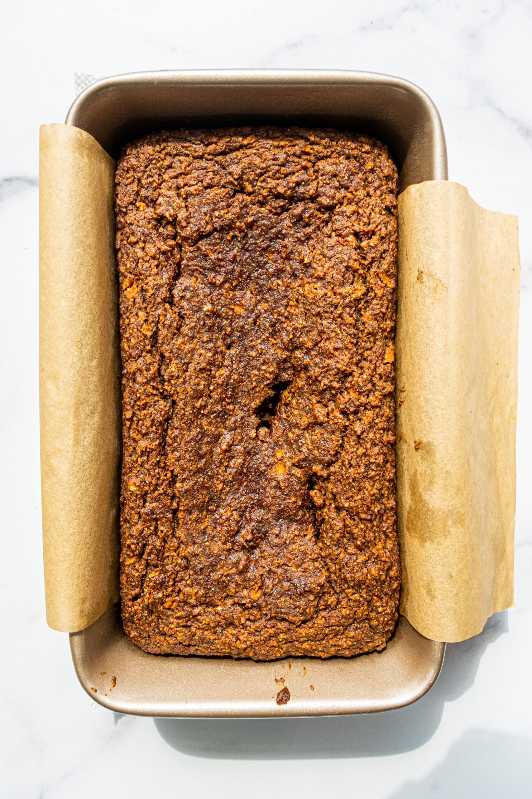 A silver loaf pan lined with parchment paper filled with baked carrot cake.