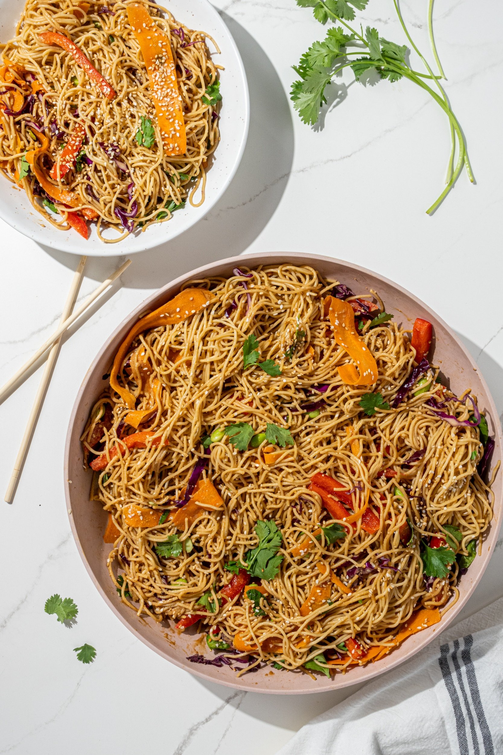 A large bowl of sesame veggie noodles and a smaller bowl of them with chopsticks.