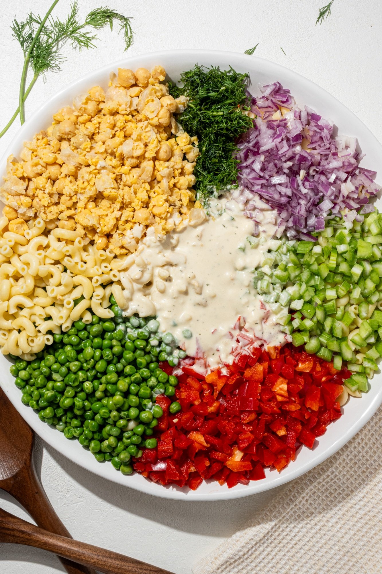 Tuna Pasta Salad in a large bowl with sprig of fresh dill and two wooden salad tongs beside it.
