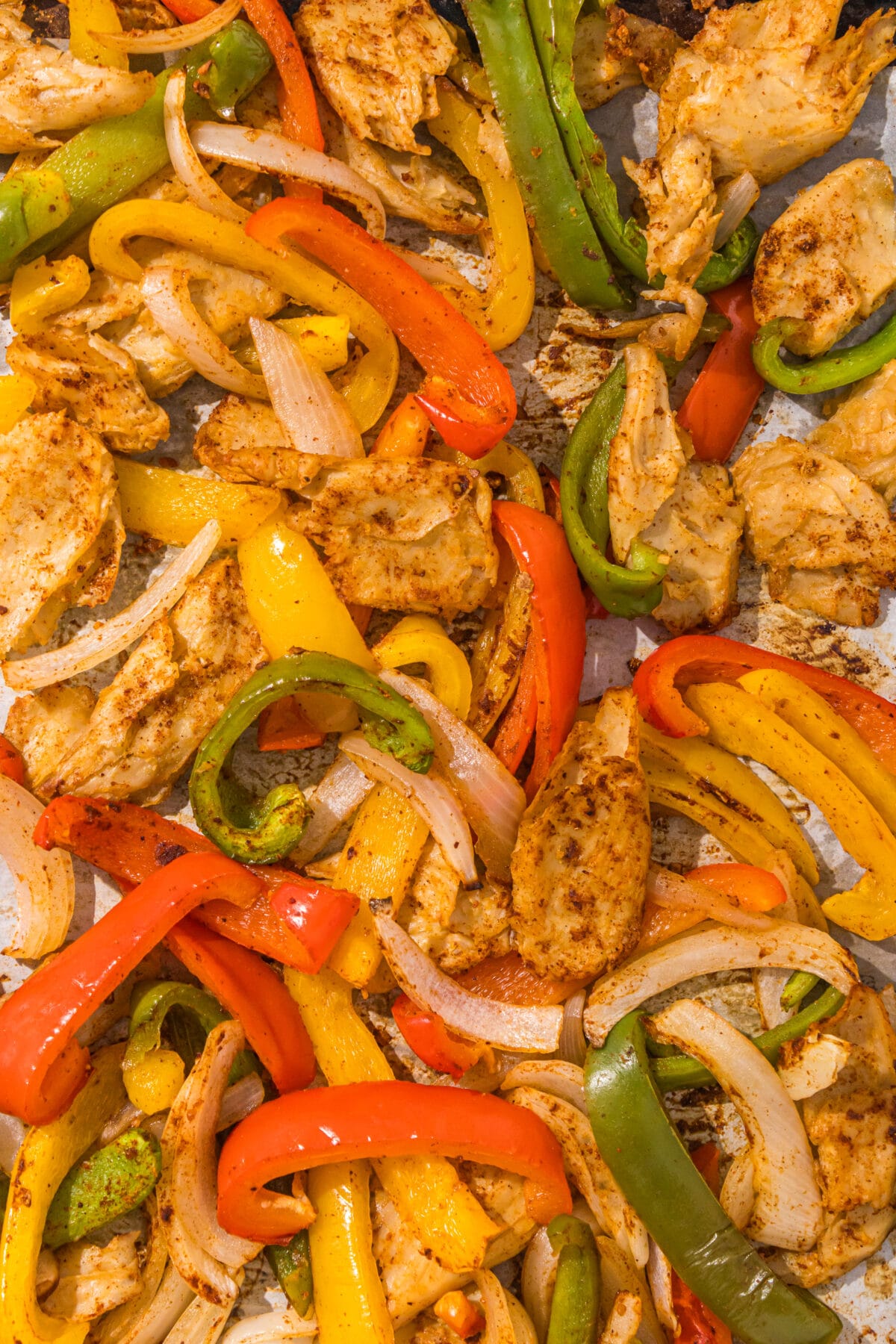 Fajitas (red, green, and yellow bell peppers, sliced onions, and chicken pieces) on a sheet of parchment paper.