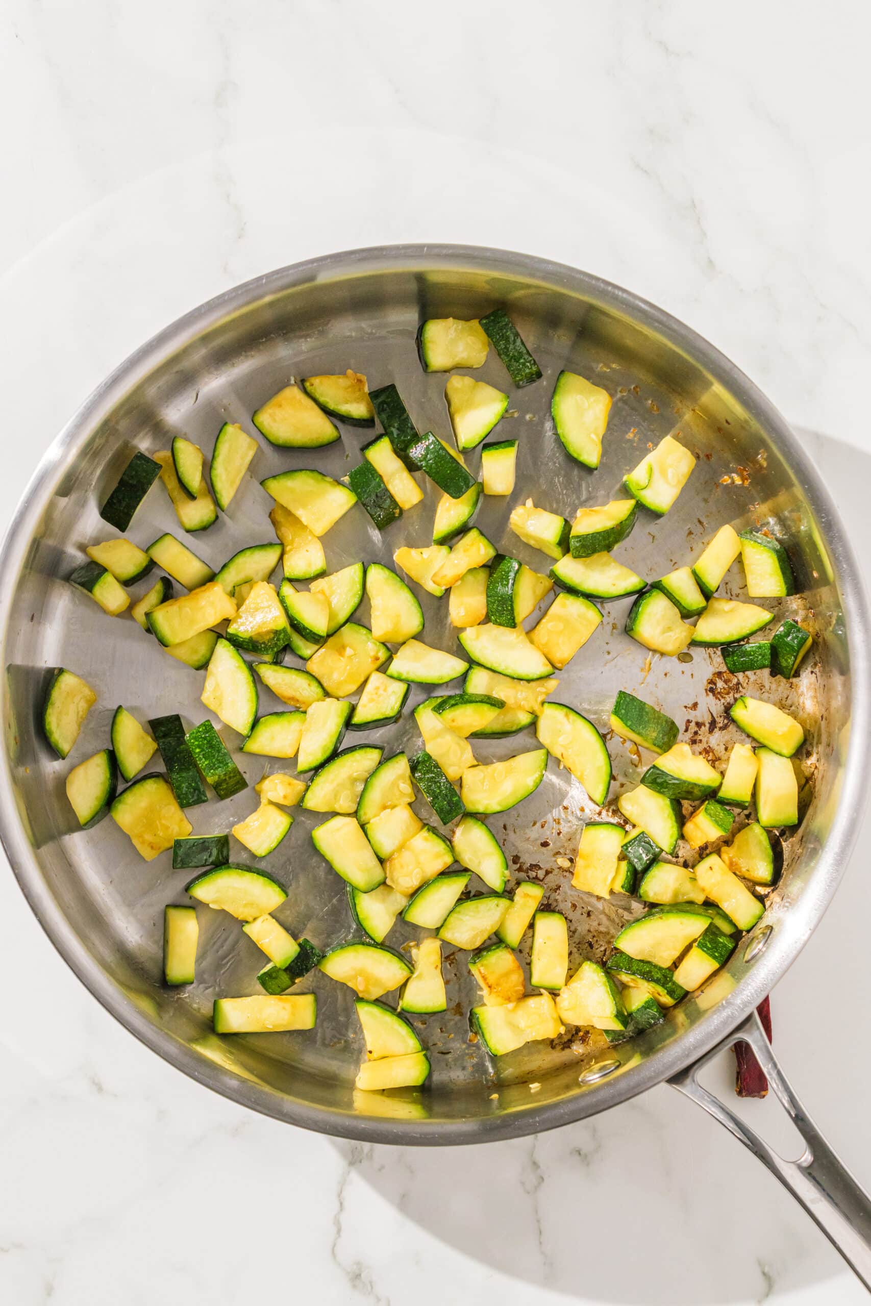 A silver pan filled with chopped zucchini being sauteed.