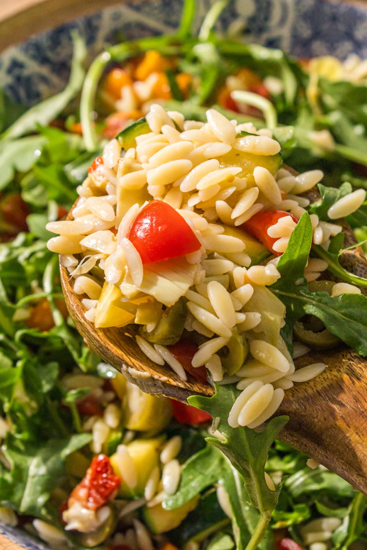 Close up of the mediterranean orzo salad with a wooden spoon in the center holding a large scoop of the salad.