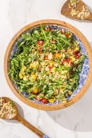 Mediterranean Orzo Salad in a large wooden salad bowl with two salad tongs beside the bowl covered in orzo.