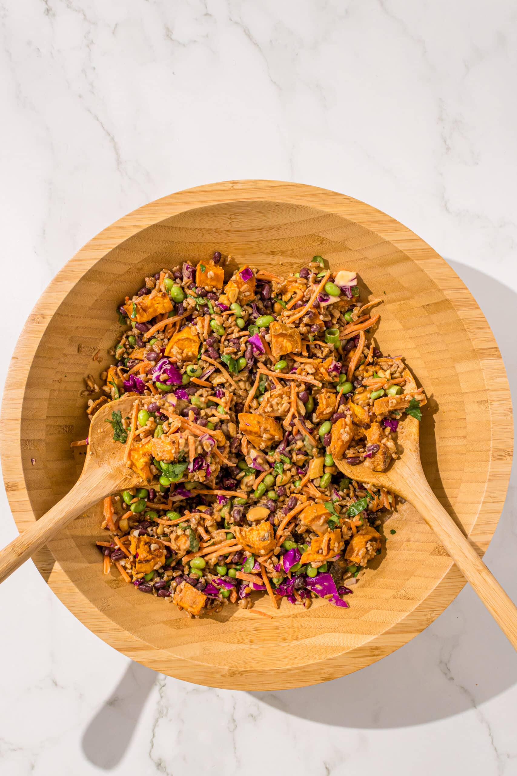 A large wooden salad bowl filled with adzuki bean farro salad and a set of wooden salad tongs.