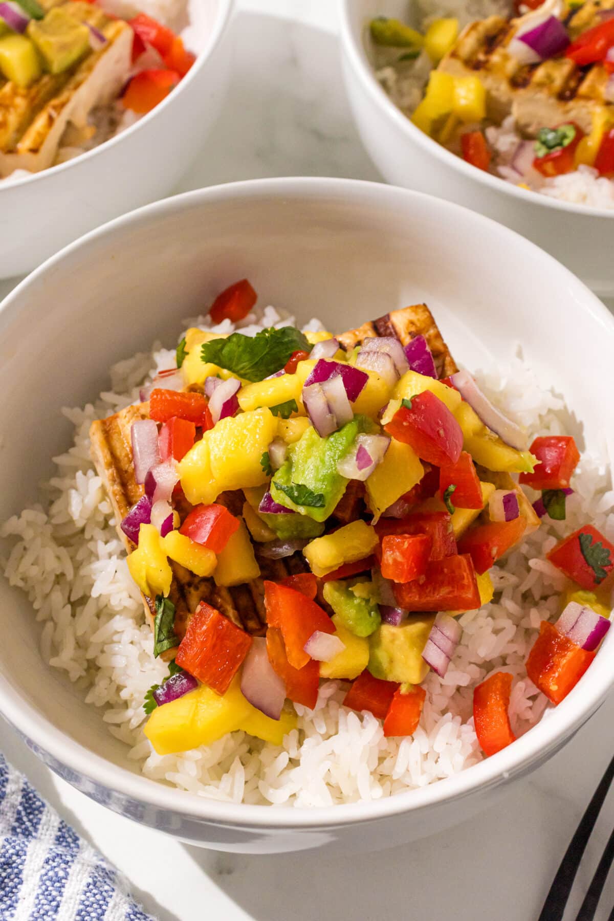 Three bowls of tofu, rice, and mango salsa. A blue and white stripe towel in the background.