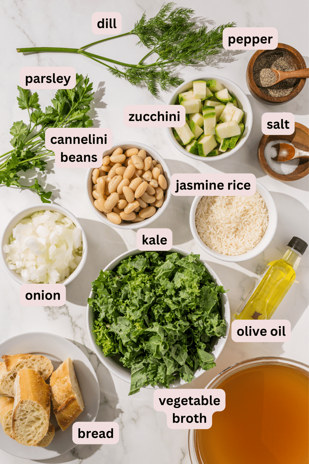 Ingredients laid out on a counter in bowls and labeled including: fresh dill, salt and pepper, zucchini, fresh parsley, cannellini beans, jasmine rice, olive oil, vegetable broth, bread, kale, and white onion.
