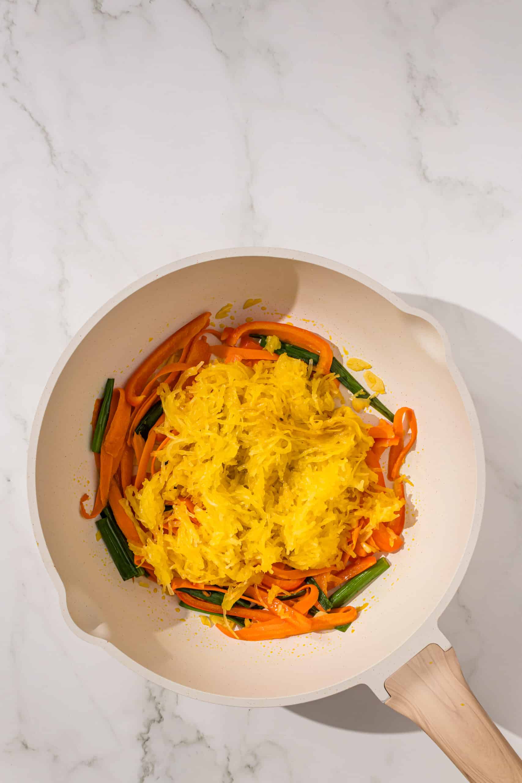 A small frying pan filled with sauteed veggies, carrots, peppers, and scallion, and a scoop of spaghetti squash on top.