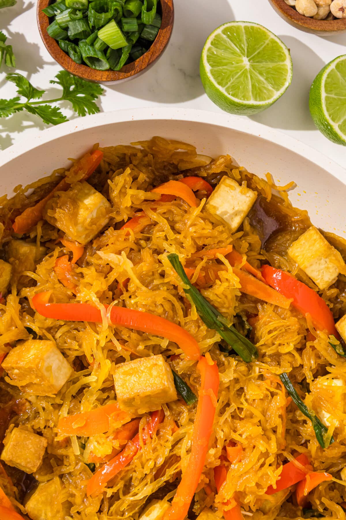 Spaghetti squash stir fry in a pan, two lime halves, and a bowl of green onions.