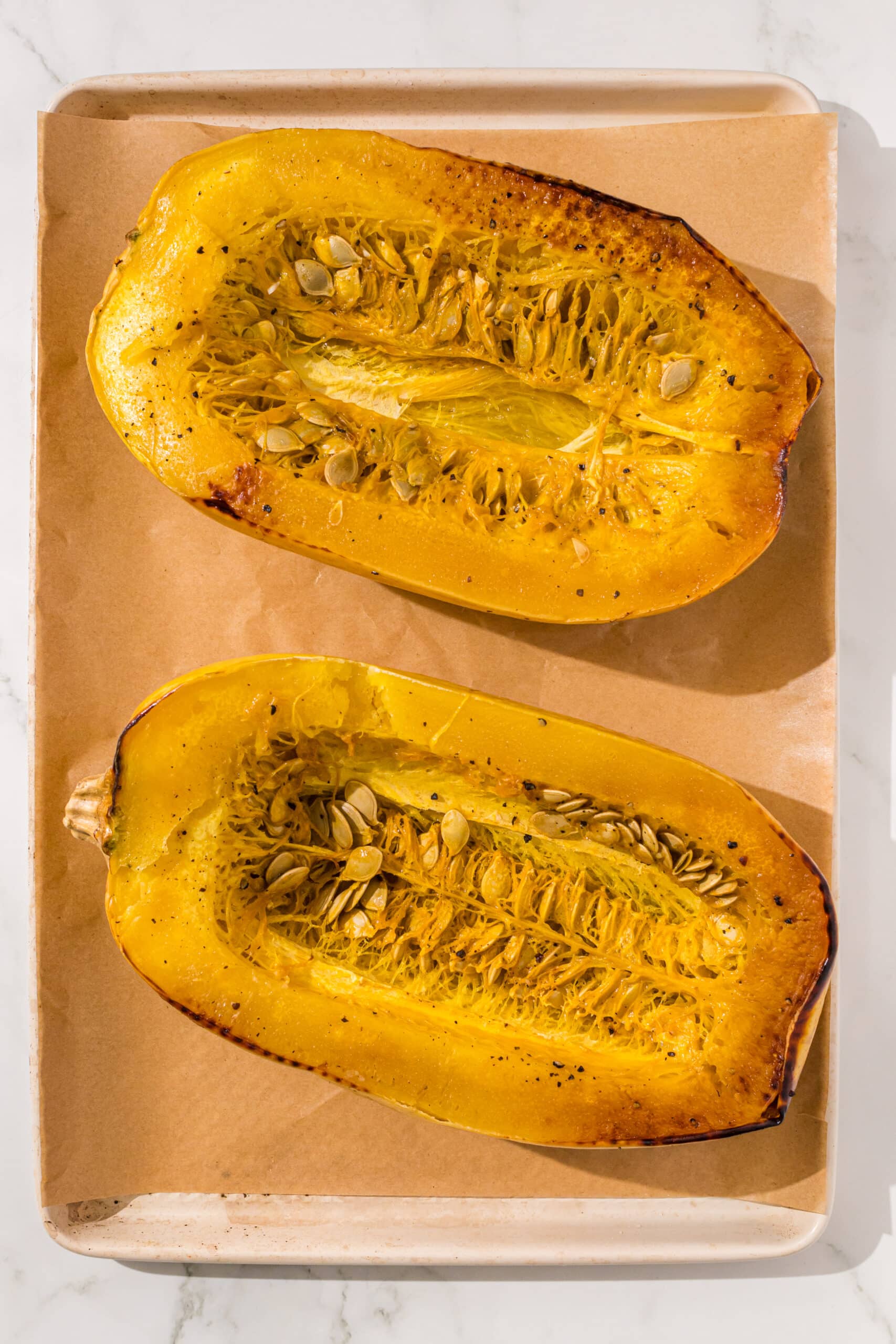 Two halves of a spaghetti squash on a baking pan lined with parchment paper.