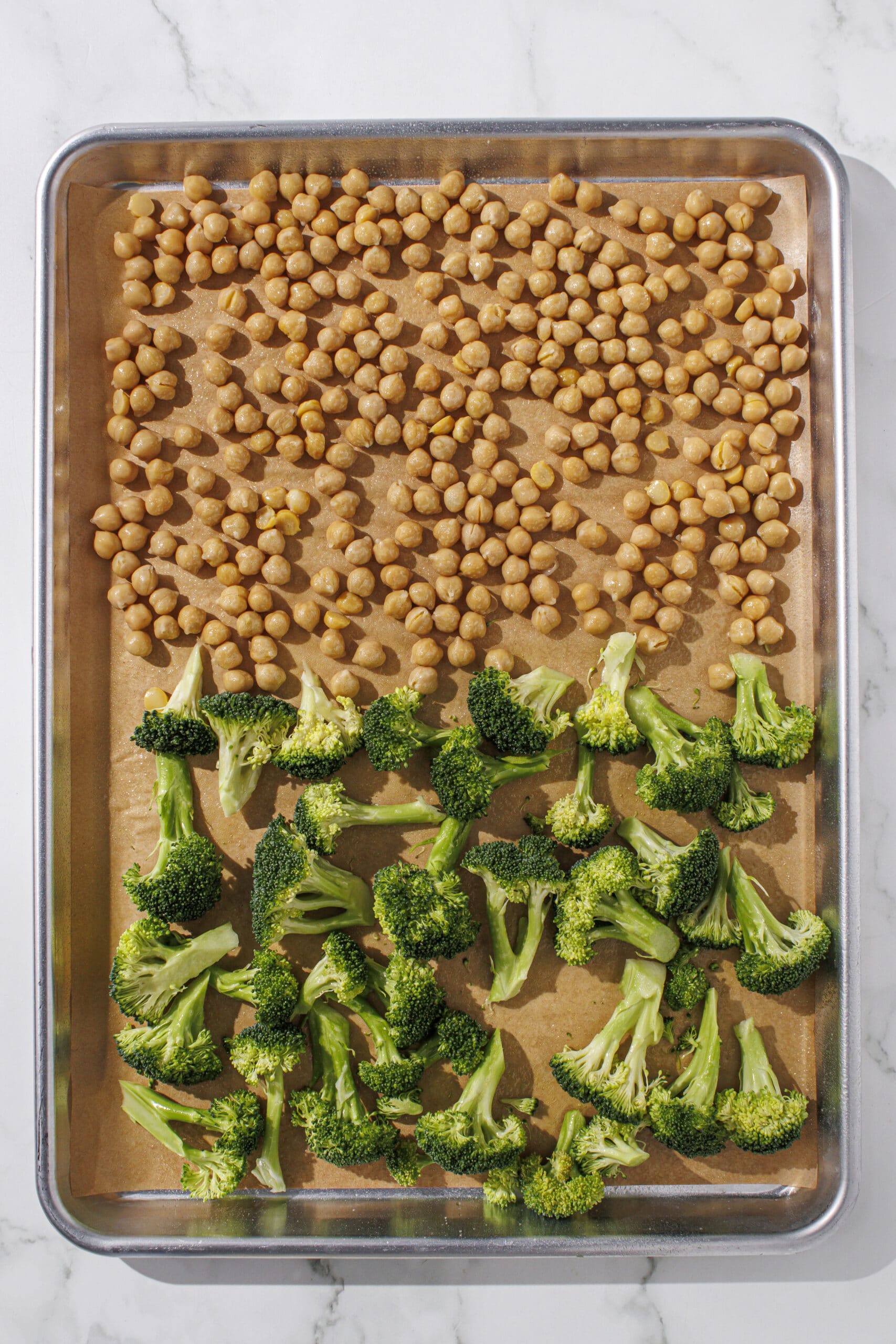 a silver pan lined with brown parchment paper filled with half chickpeas and half chopped broccoli.