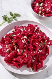 A white plate filled with a pink pasta topped with cheese, parsley, and pine nuts.