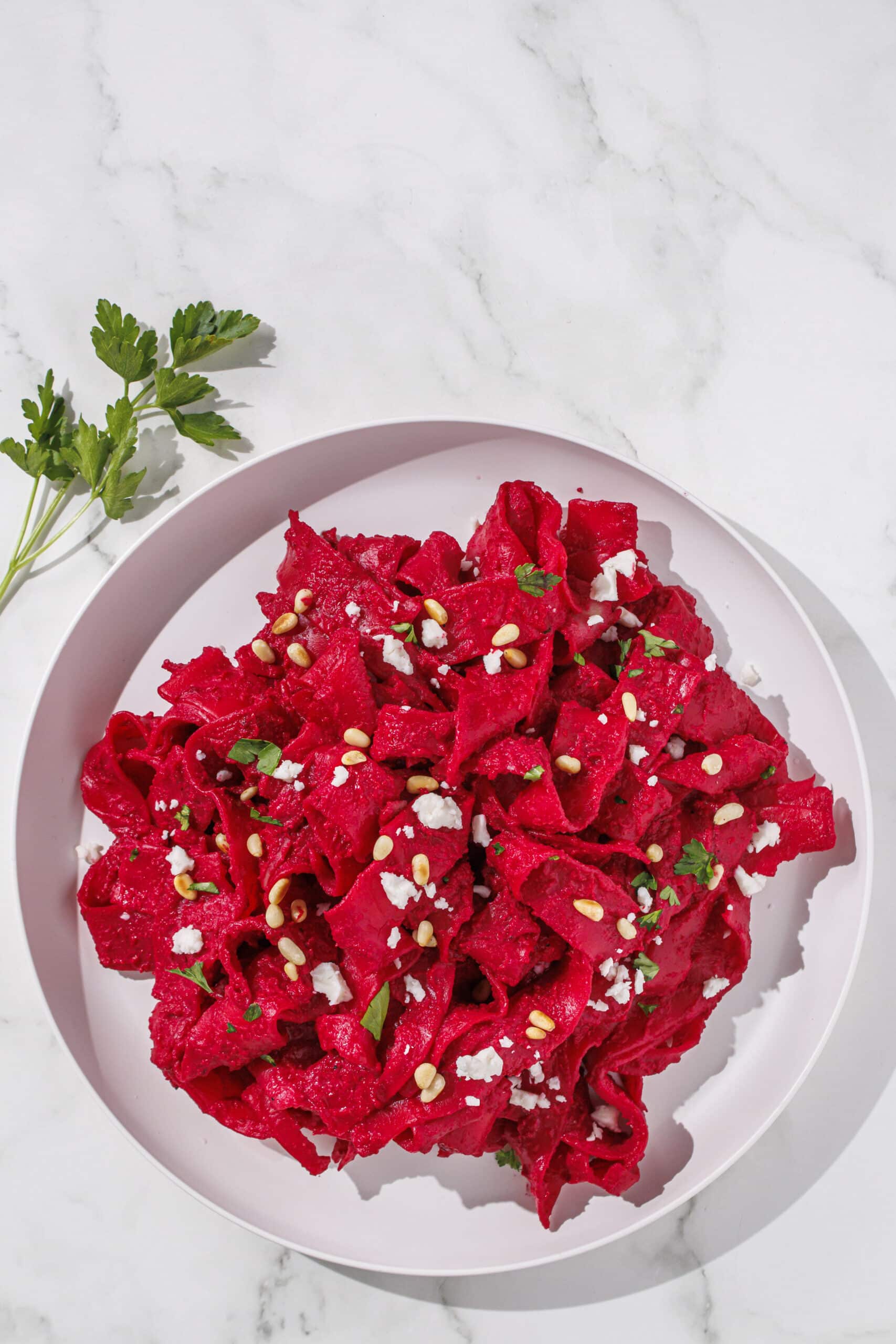 A plate of pink pasta topped with parsley, pine nuts, and feta.