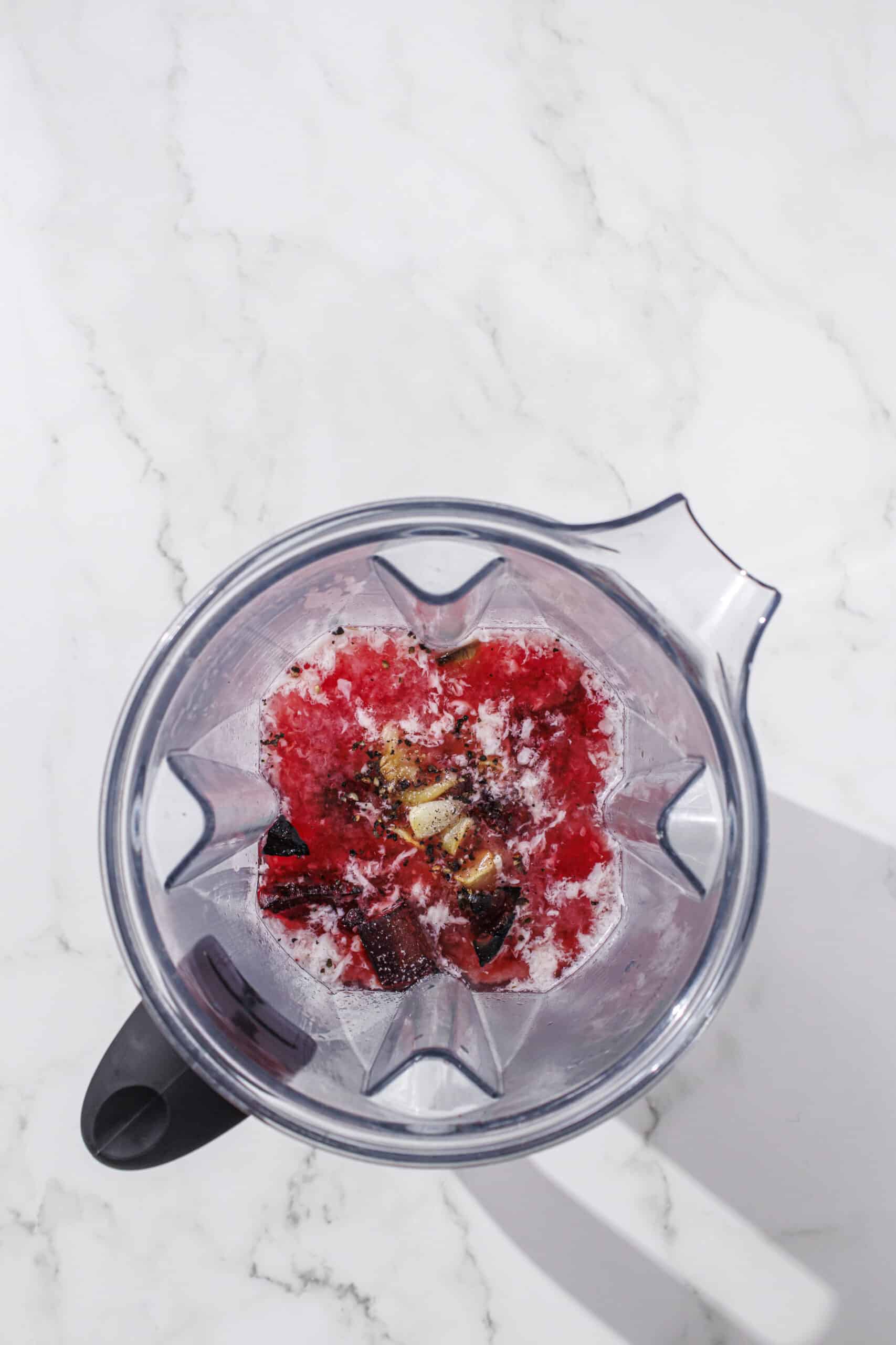 A blender filled with beets, cashews, milk, pasta water, garlic, lemon juice, and salt/pepper.