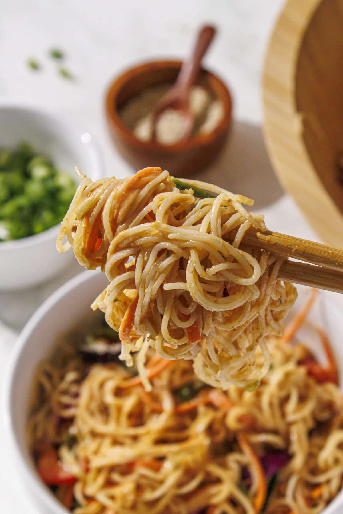 A set of chopsticks holding peanut noodles with veggies in it.