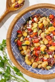 Mediterranean Gnocchi in a large brown wood & blue bowl. To the left of the bowl is parsley and a wooden spoon.