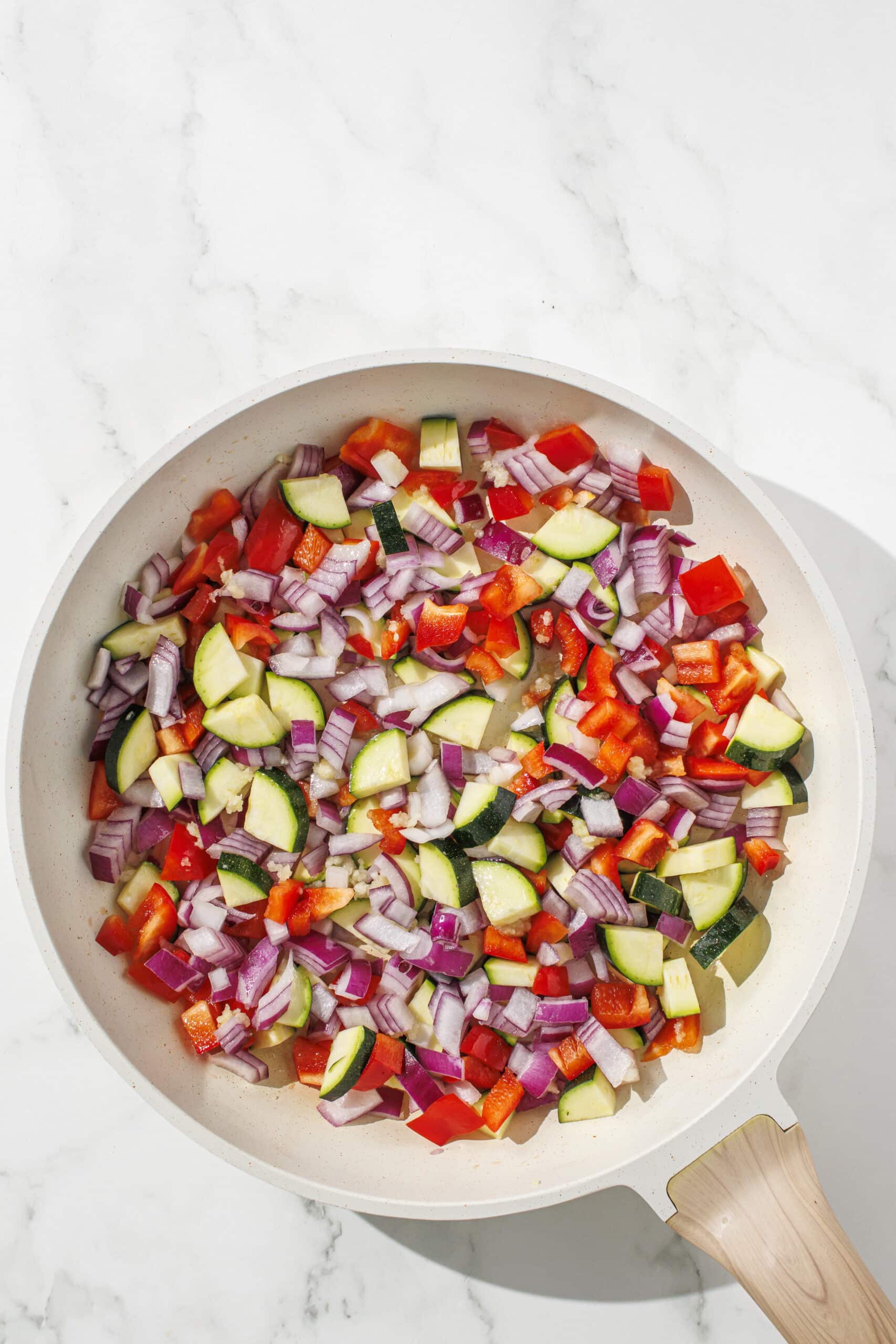 A small white pan filled with zucchini, bell pepper, and red onion getting ready to be cooked.