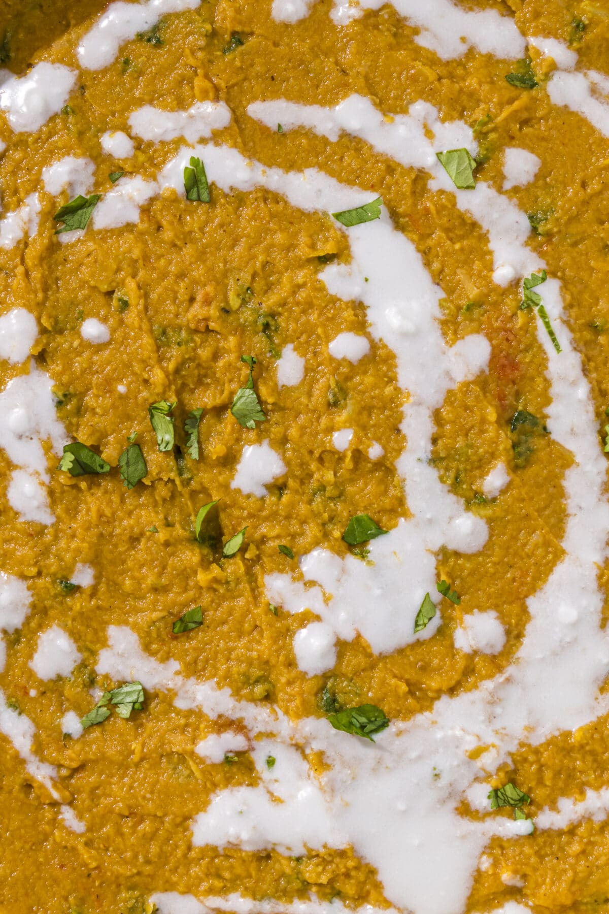 Close up of a yellow curry with a white cream sauce drizzled on top and fresh parsley.
