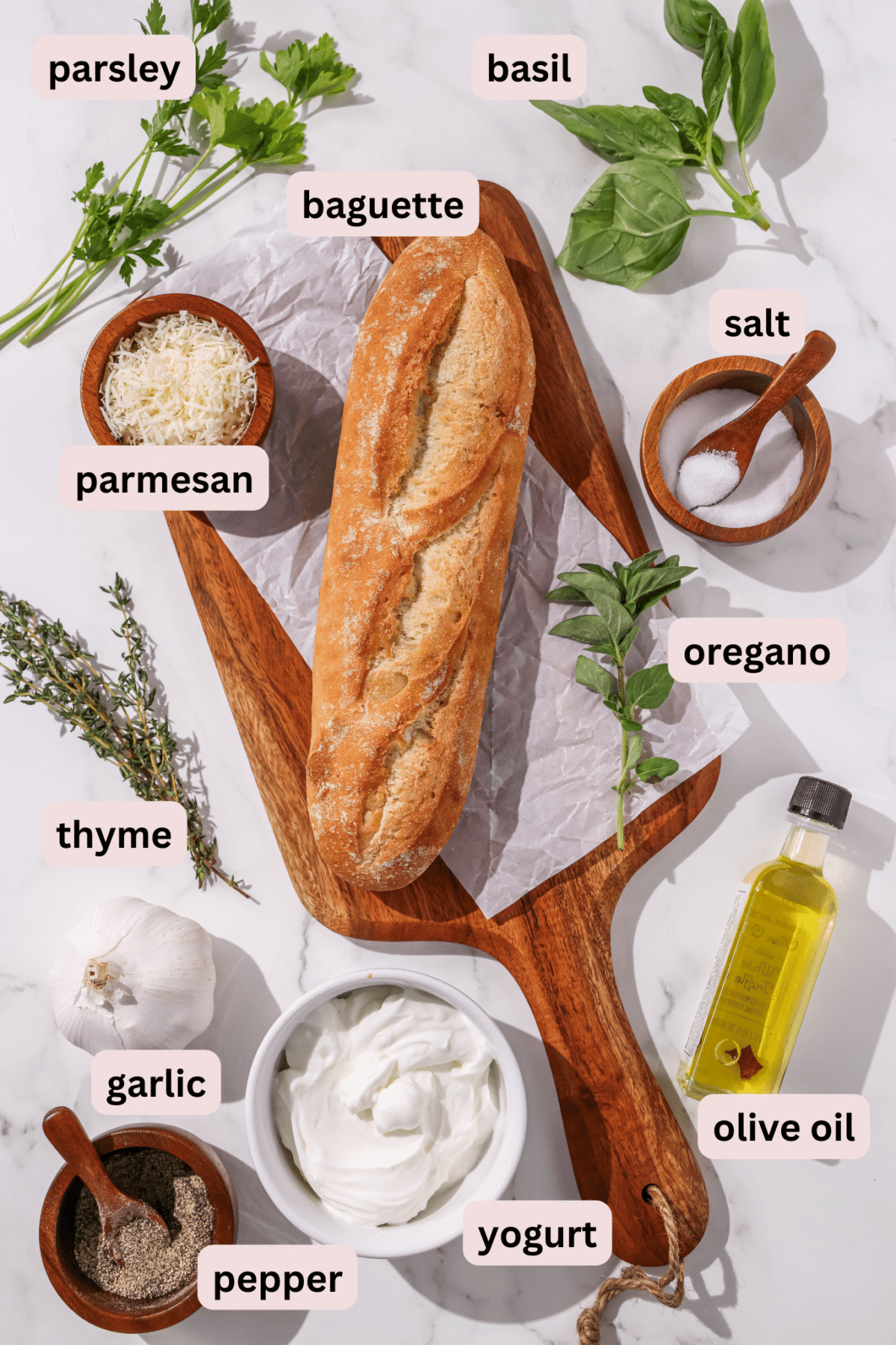 Ingredients laid out on a counter and labeled including: parsley, basil, baguette, salt, parmesan, oregano, oil, yogurt, garlic, thyme, and black pepper.