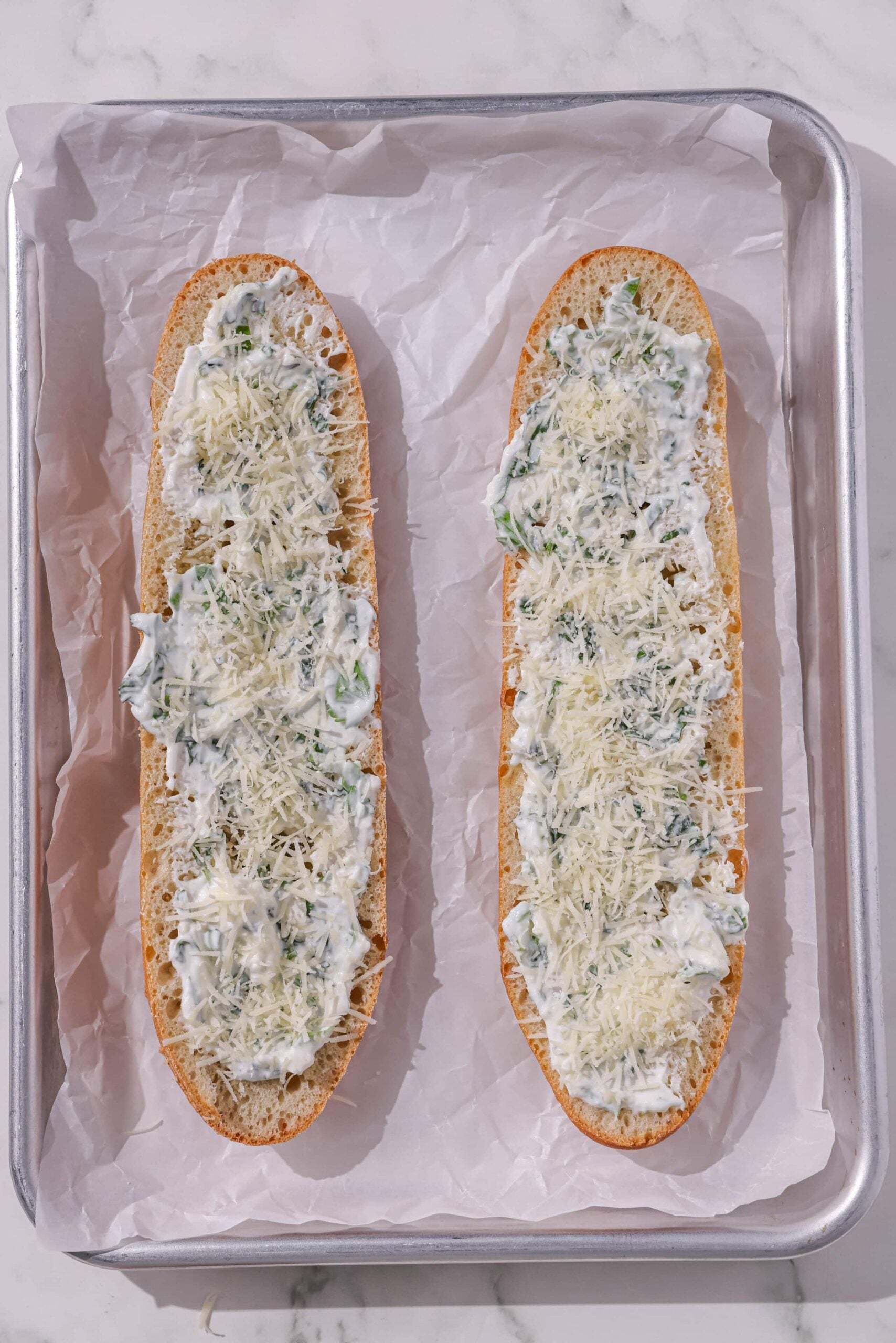 Two loaves of garlic bread ready to be baked on a pan lined with parchment paper.