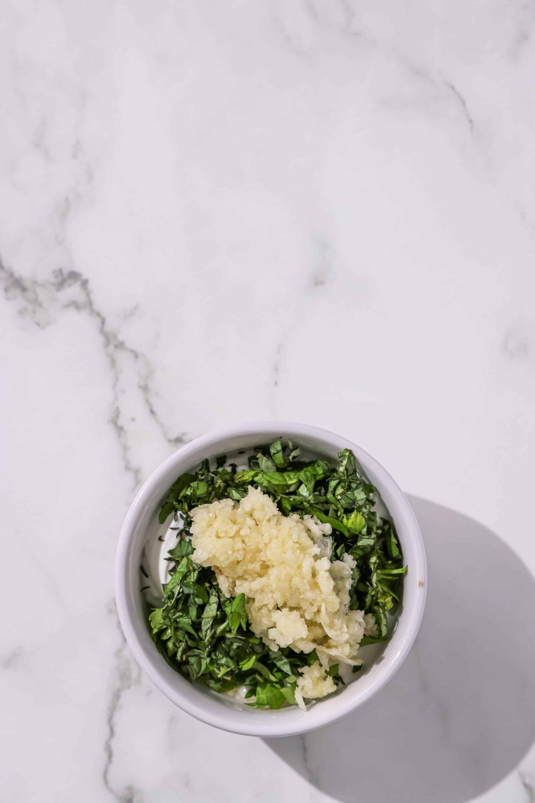 A small bowl of yogurt with fresh herbs and minced garlic.