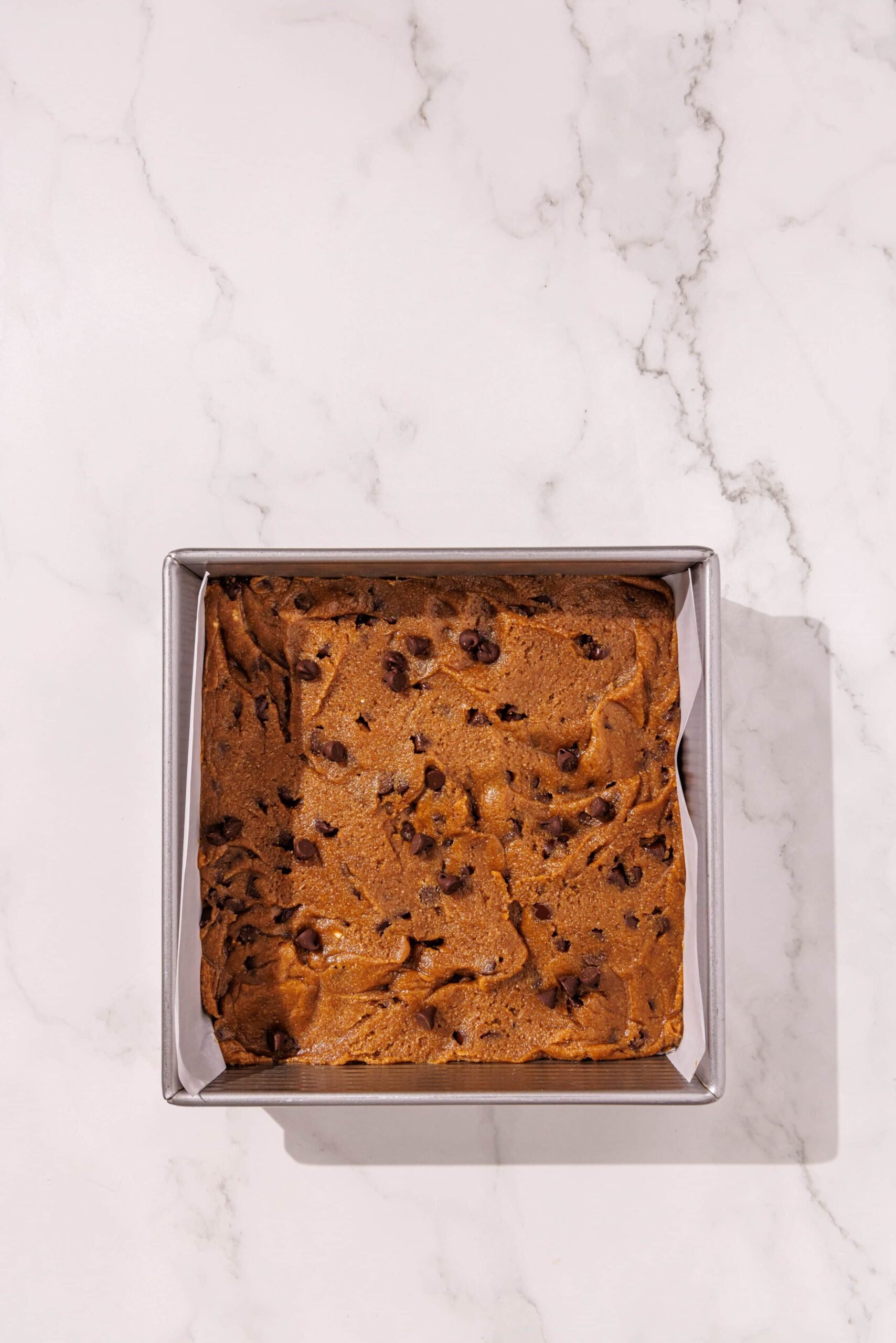 A lined 8x8 silver baking pan filled with vegan tahini blondies raw.