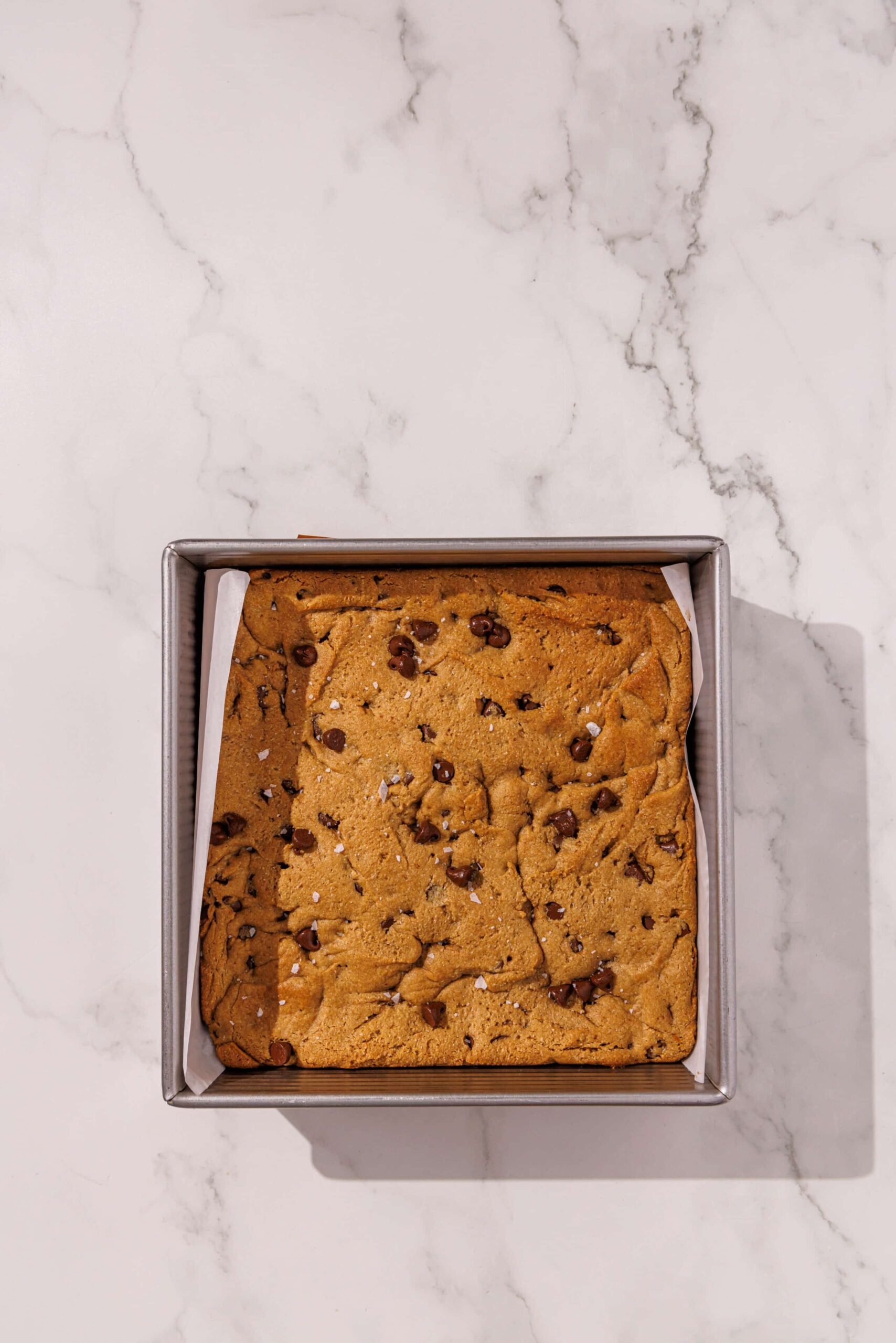 An 8x8 baking pan lined with parchment paper and filled with vegan tahini blondies.