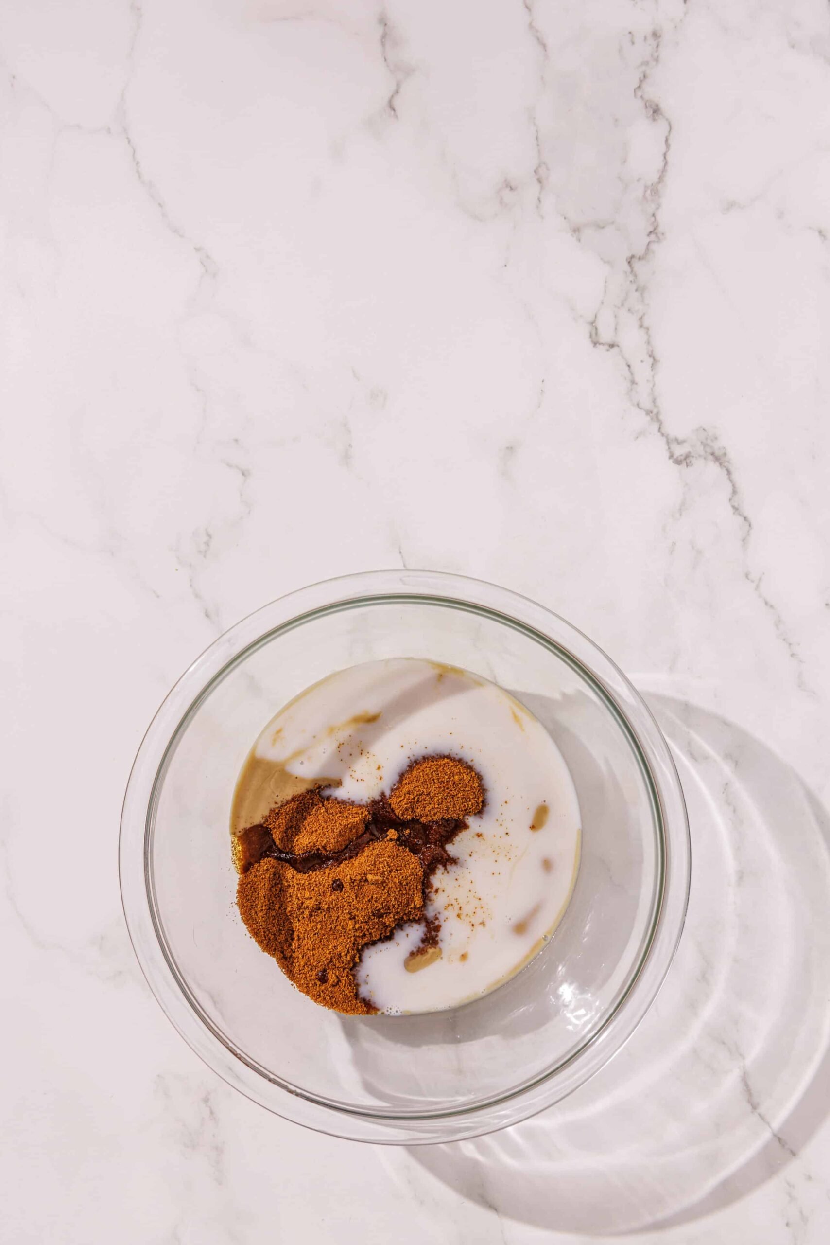 A glass bowl filled with almond milk, tahini, coconut sugar, maple syrup, and vanilla.